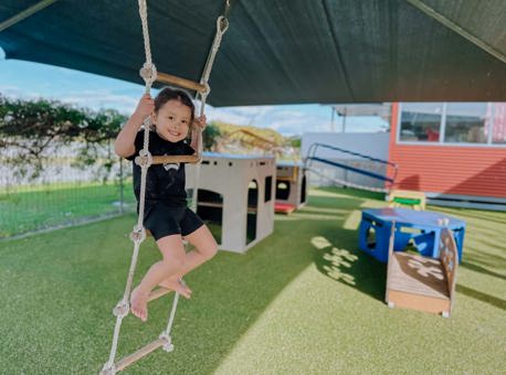 Evolve Education Preschool girl playing on ladder in playground at daycare